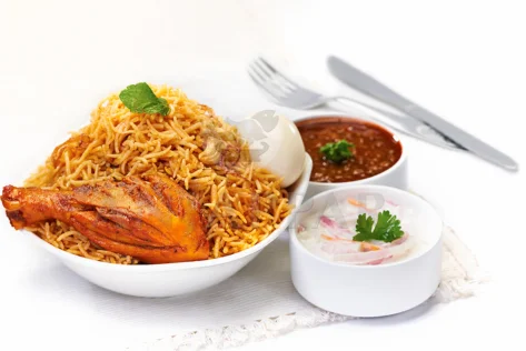 A bowl of delicious steaming chicken briyani with aromatic spices served with onion raitha & gravy.