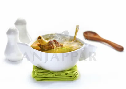 A bowl of creamy mutton soup with aromatic spices served in white hemoton bowl with salt & pepper.