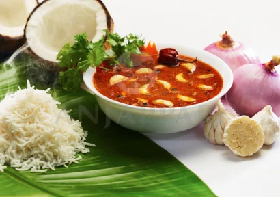 A bowl of garlic tangy curry with hot steamed rice served on a banana leaf accompanied with onion.