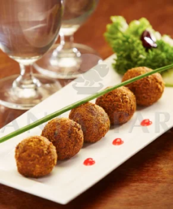 A  white plate is filled with chicken balls garnished by lettuce and sauce & two glasses of water