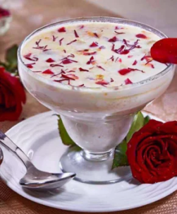 A bowl of tasty ice cream topped with beautiful red roses, presented with a silver spoon on a plate