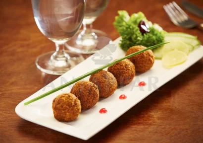 A plate of succulent chicken balls served with lemon, cilantro, spring onions, water, and cutlery