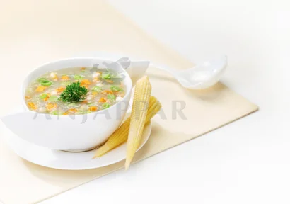 A bowl of hot veg delicious soup with corn and carrots decorated with baby corn on a table.