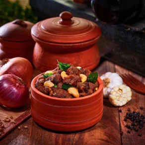 A delicious mouthwatering fried chicken served in a red clay pot with garlic,pepper and onion